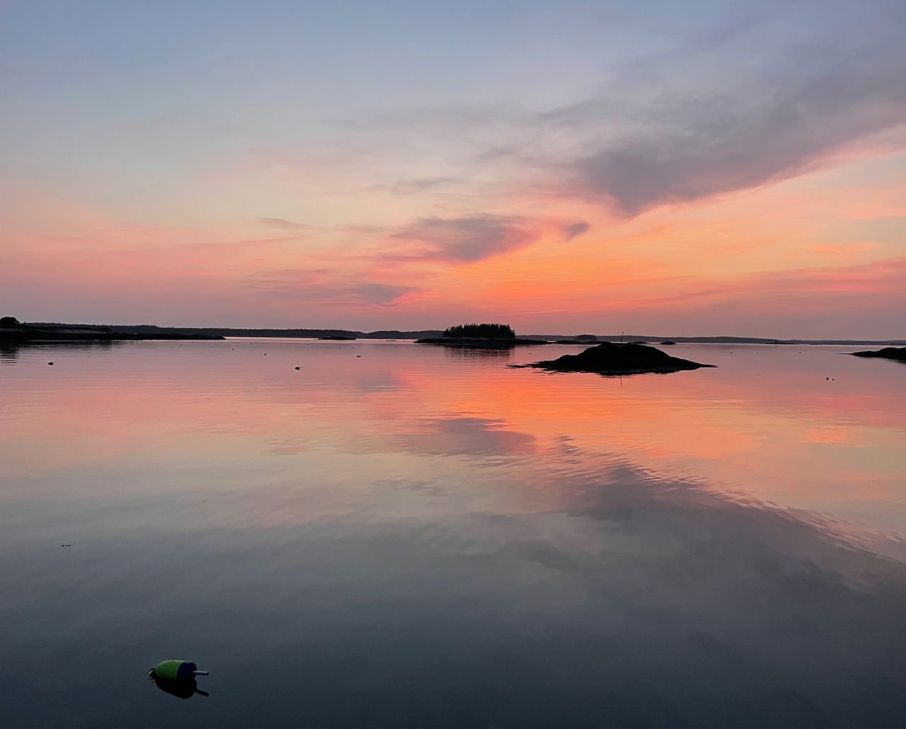 Sunset over calm water at Mistake Island, Maine, with small island silhouettes and peach clouds reflected in the water.