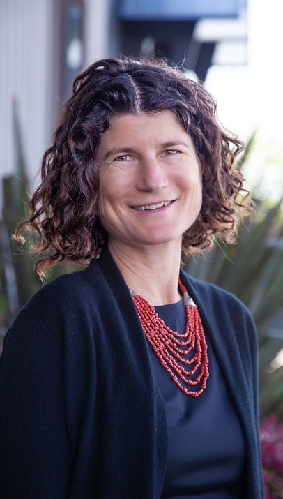 Portrait of Eliza Patten, smiling warmly, wearing a red beaded necklace.